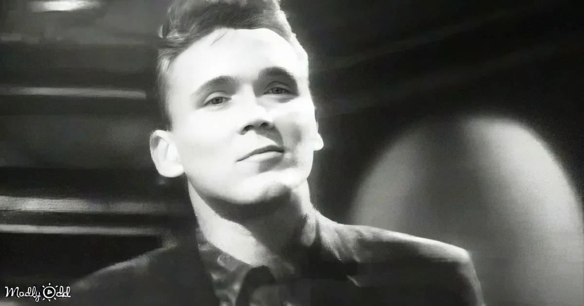 A man in a suit and tie, looking upward, with a blurred background and a watermark in the corner.