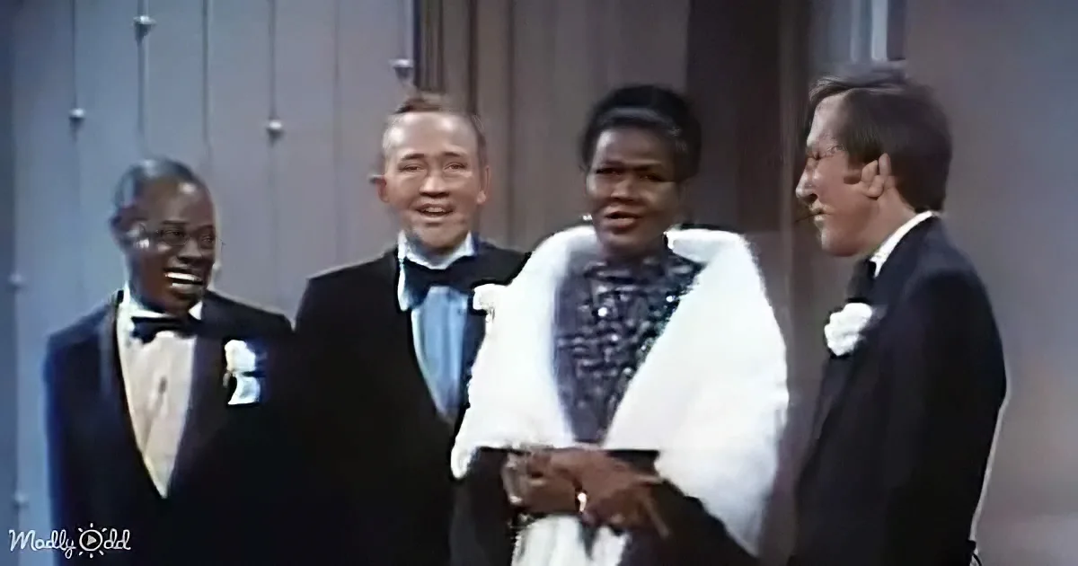 A group of four people in formal attire, including a woman in a white fur coat, are smiling and interacting on stage.