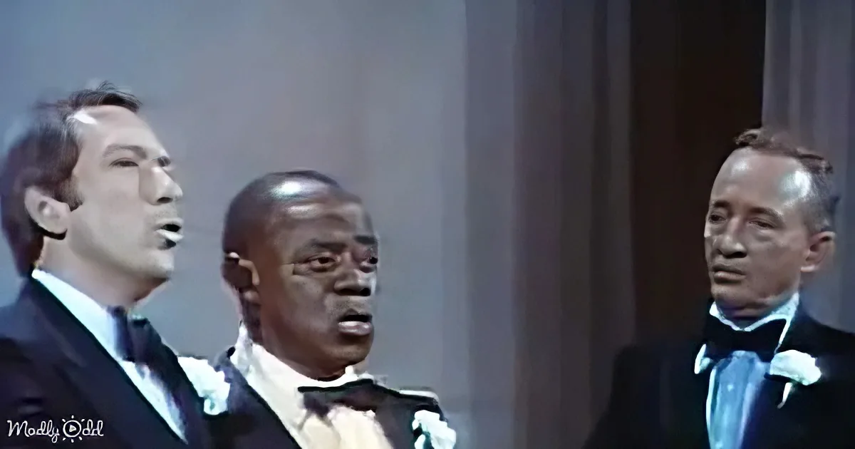 Three men in formal attire sing together, one wearing a bow tie, against a plain backdrop.