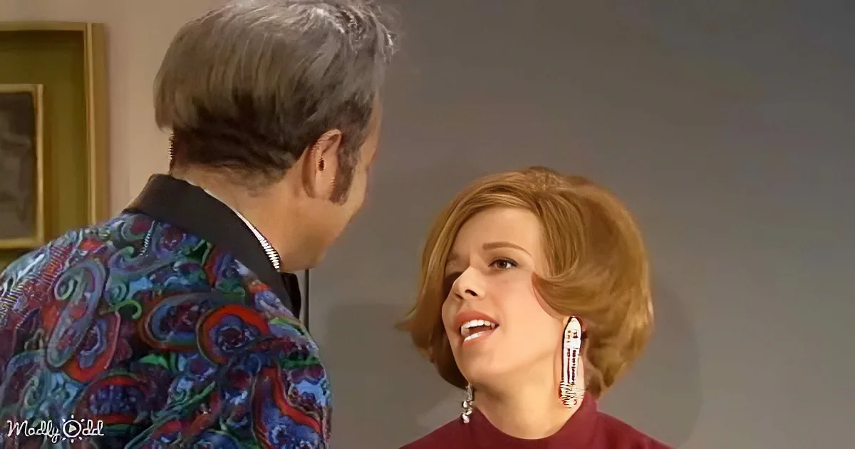 A woman with short, styled hair and large earrings is looking at a man in a colorful patterned shirt.