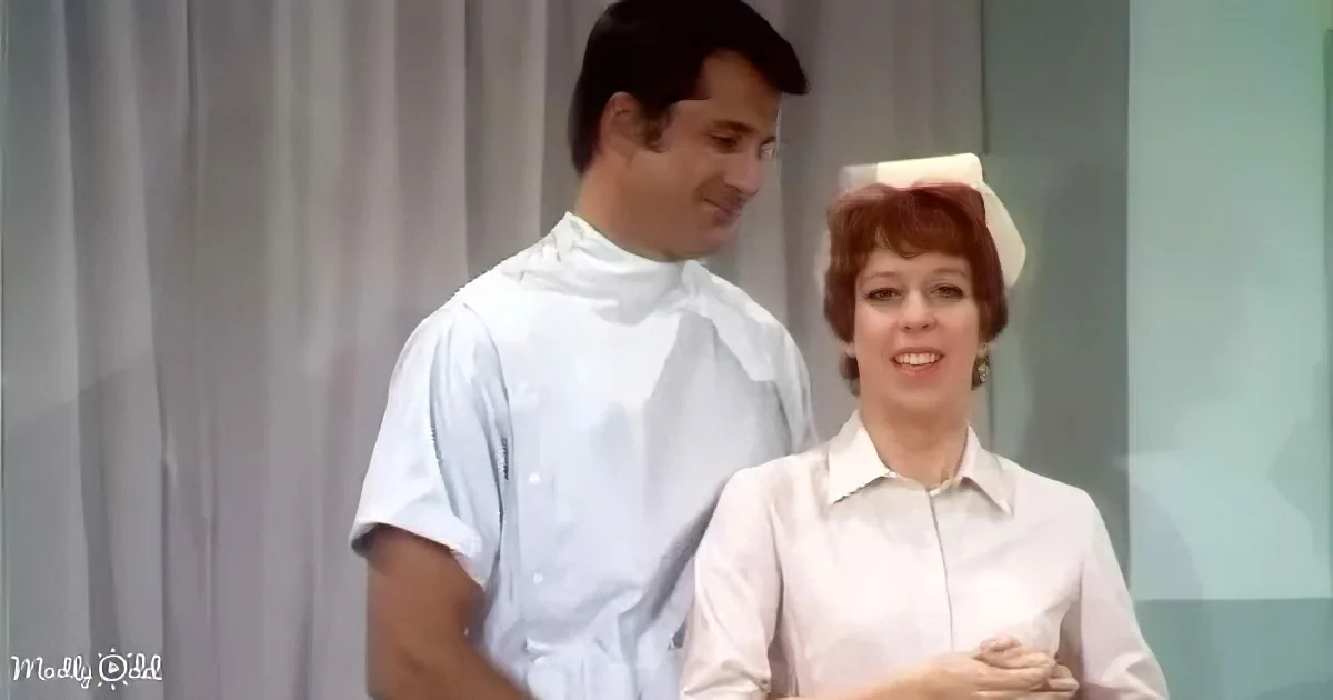 A man in a white shirt smiles as a woman in a nurse's uniform looks up, both in a clinical setting.