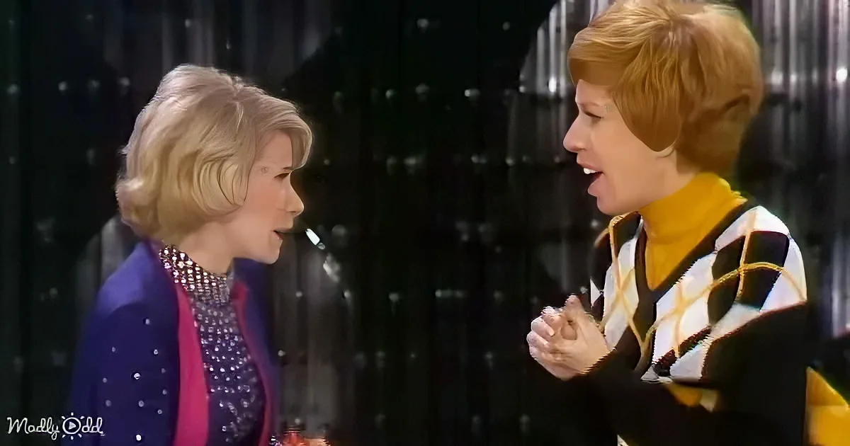 Two women are engaged in conversation, one with blonde hair and a purple jacket, the other with red hair and a patterned...