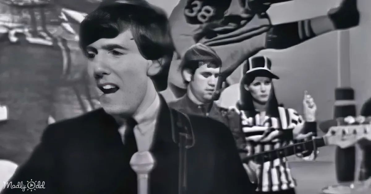 A man in a suit sings into a microphone, with a band and referee in the background.