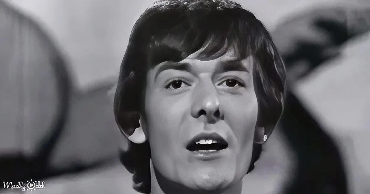 A person with short, dark hair and a surprised expression is the main subject of this black-and-white image.