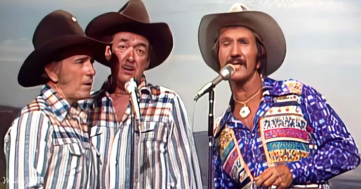 Three men in cowboy hats and plaid shirts sing into microphones, one wearing a colorful patterned shirt.