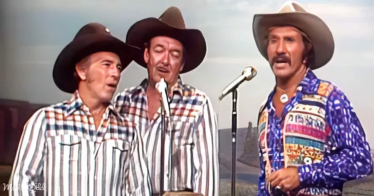 Three men in cowboy hats and plaid shirts sing into microphones, one holding a guitar.