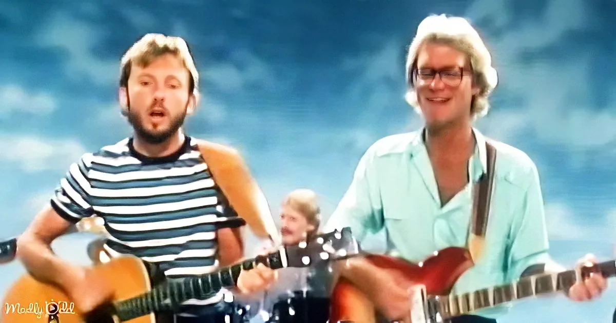 Two musicians play guitars against a blue sky backdrop, one in a striped shirt, the other in a light green shirt.