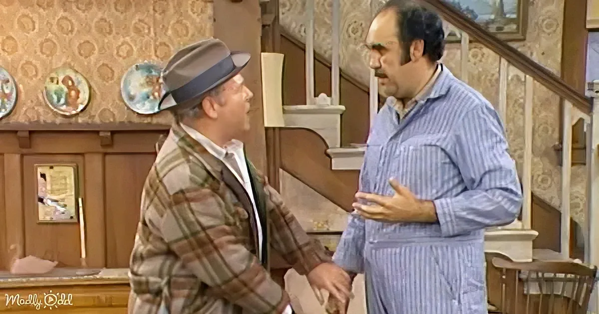 Two men in a room, one in plaid jacket, the other in striped pajamas, appear to be having a conversation.