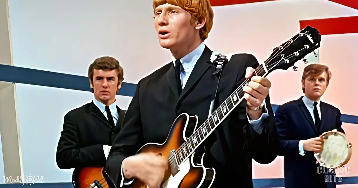 A man in a suit plays a guitar, surrounded by two other men in suits, one holding a banjo.