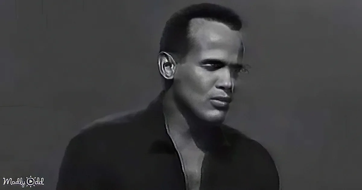 A man with short hair, wearing a dark shirt, stands against a dark background, looking to the side.