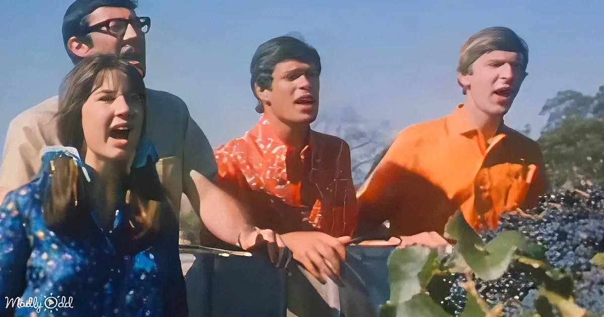 Four people, two men and two women, are singing outdoors, wearing colorful 1960s-style clothing.