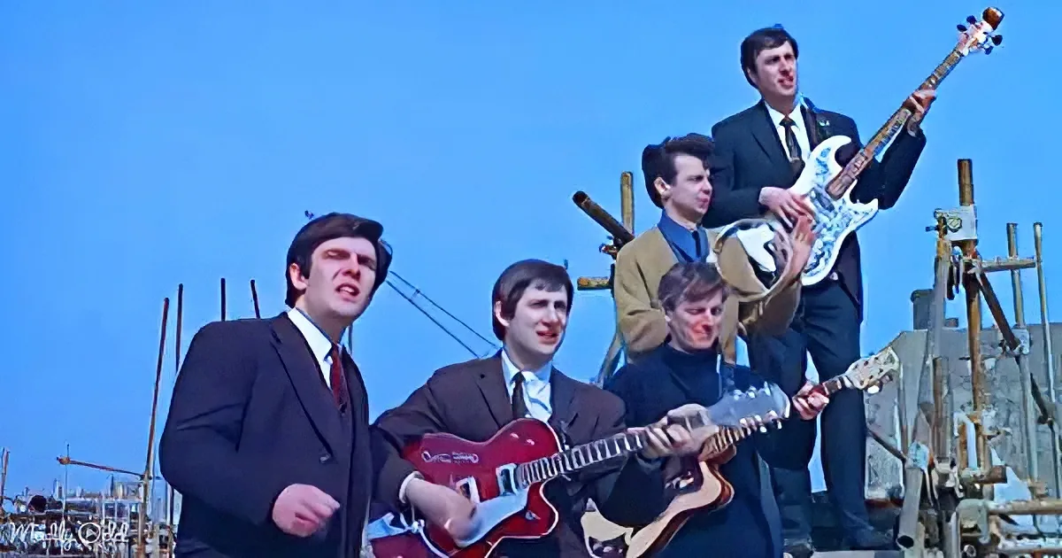 A band in suits plays guitars and sings on a construction site under a clear blue sky.