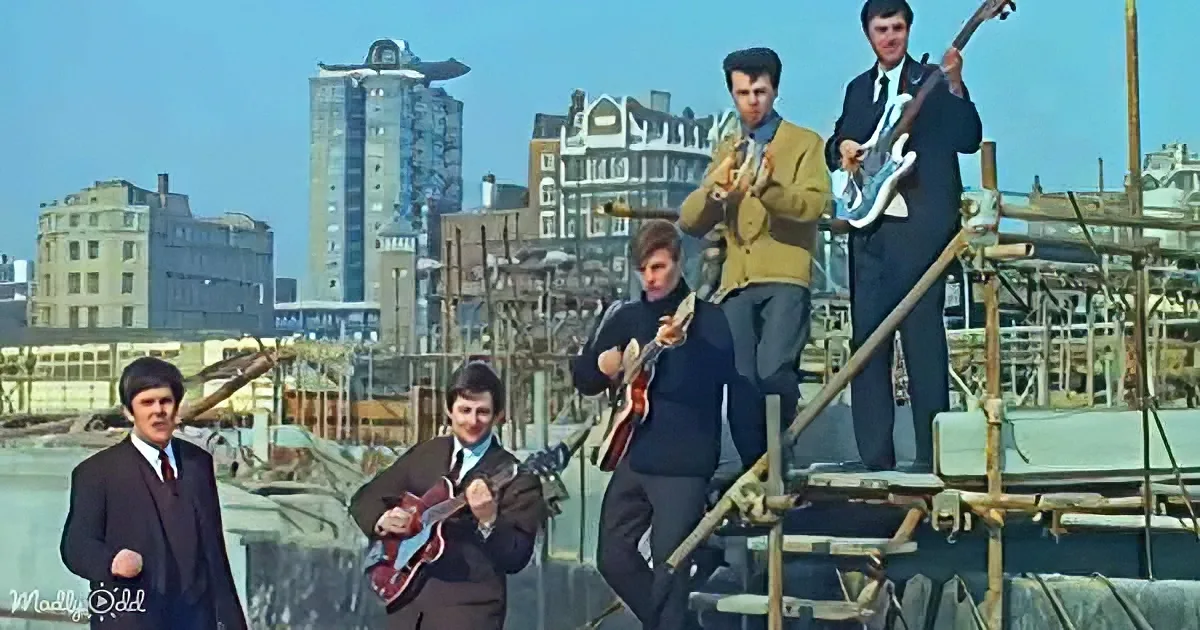 A band in suits plays instruments on scaffolding with a cityscape in the background.
