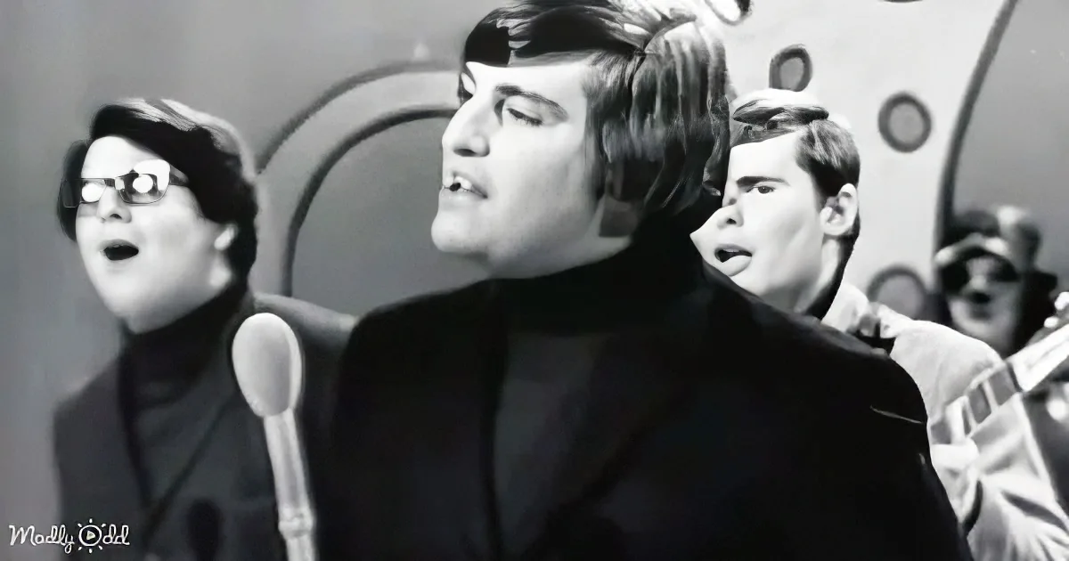 A man in a black suit sings passionately, surrounded by other musicians in a vintage setting.