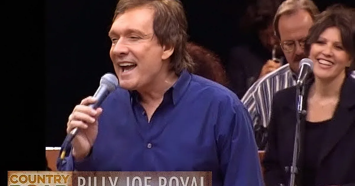 A smiling person with short brown hair and a striped shirt against a dark background.