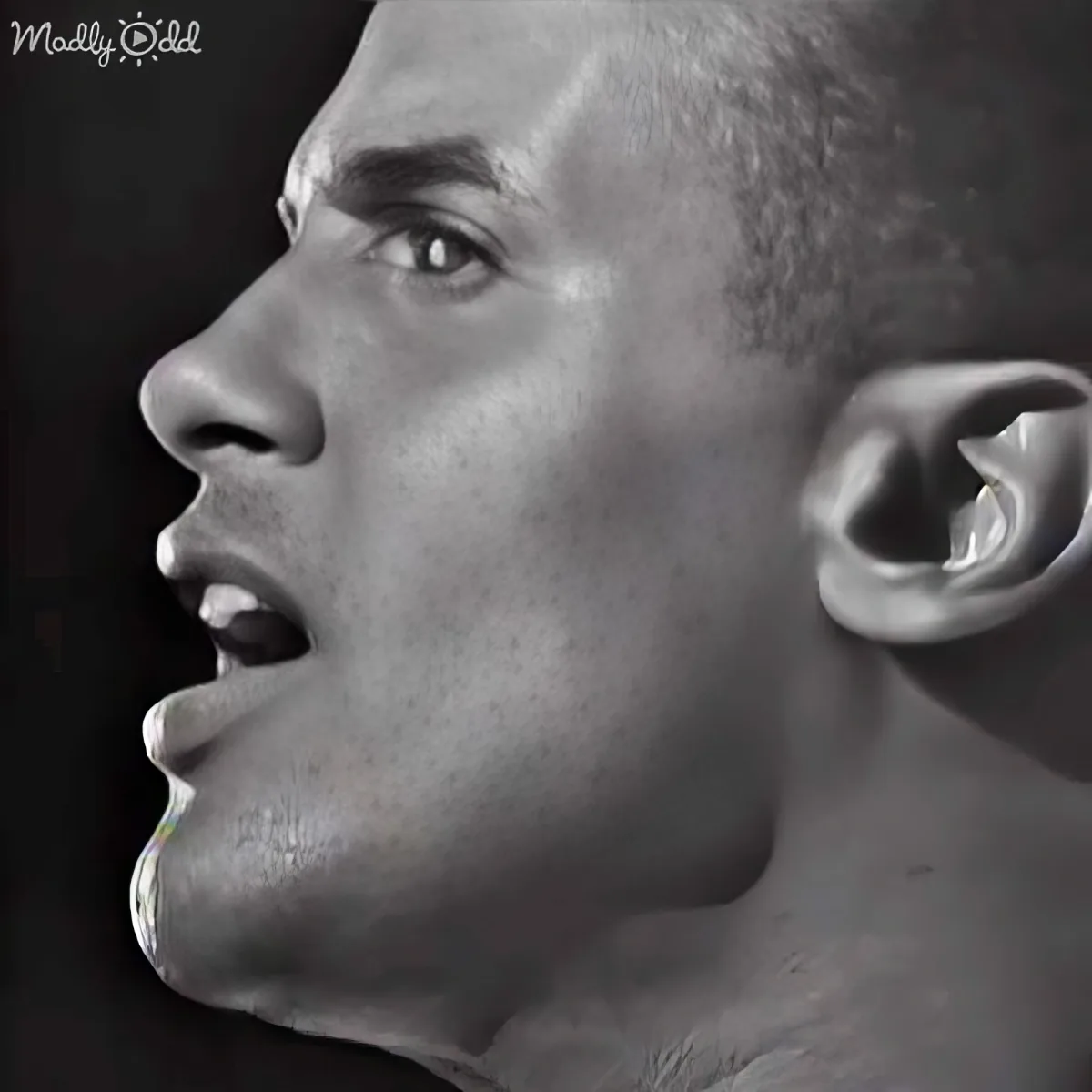A close-up of a person's face with a side profile, mouth slightly open, and a dark background.