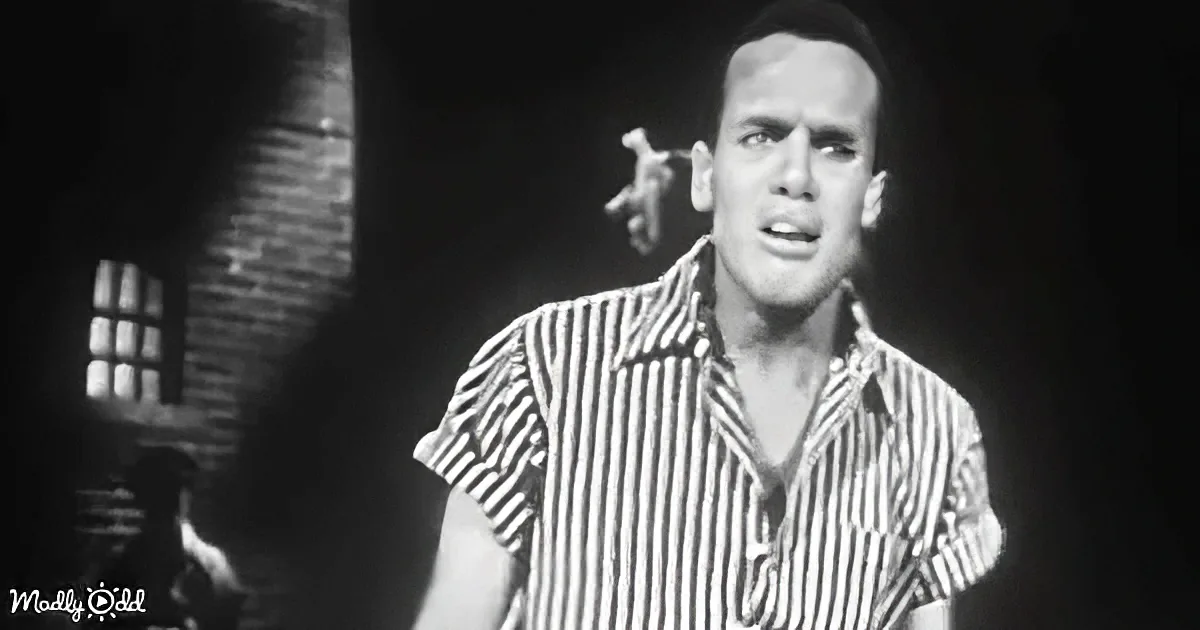 A man in a striped shirt is singing passionately in a dimly lit setting.