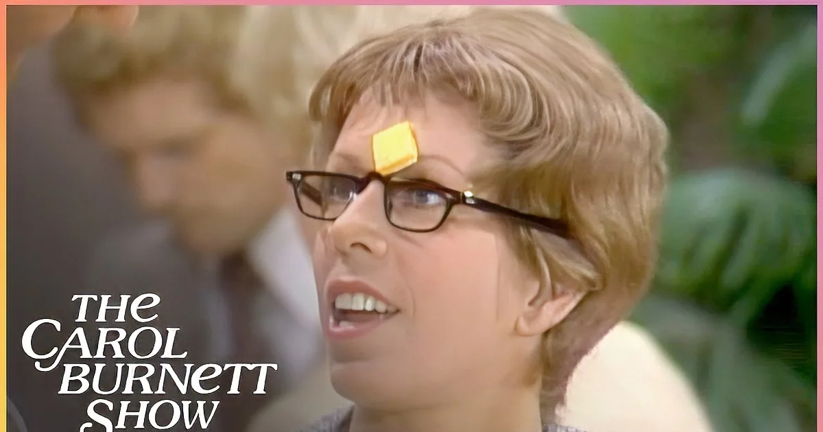A woman with glasses and a yellow object on her forehead looks up, mouth slightly open.