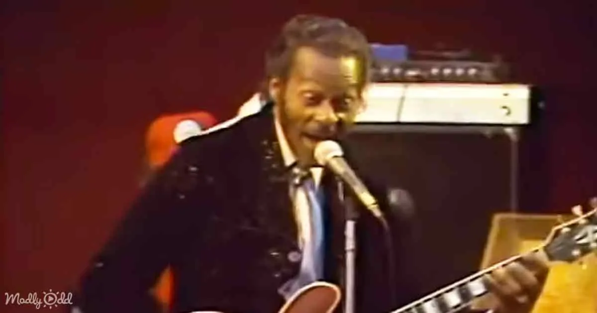 A man in a black suit plays guitar and sings into a microphone on stage.