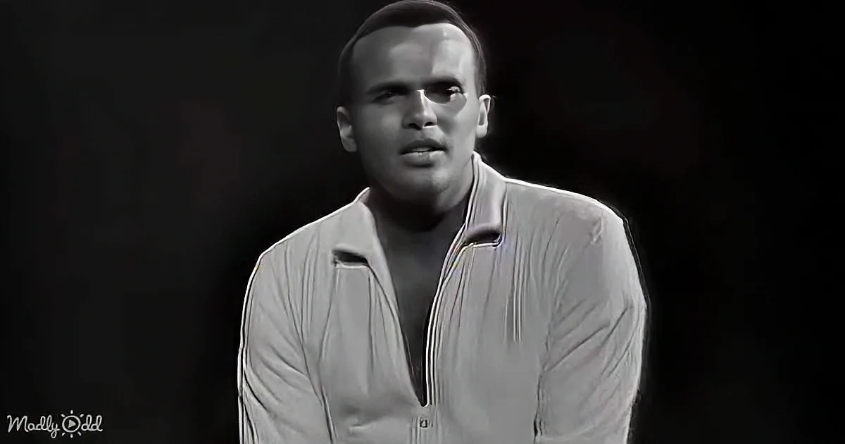 A man in a light-colored, open-collared shirt sits against a dark background, looking slightly to the side.