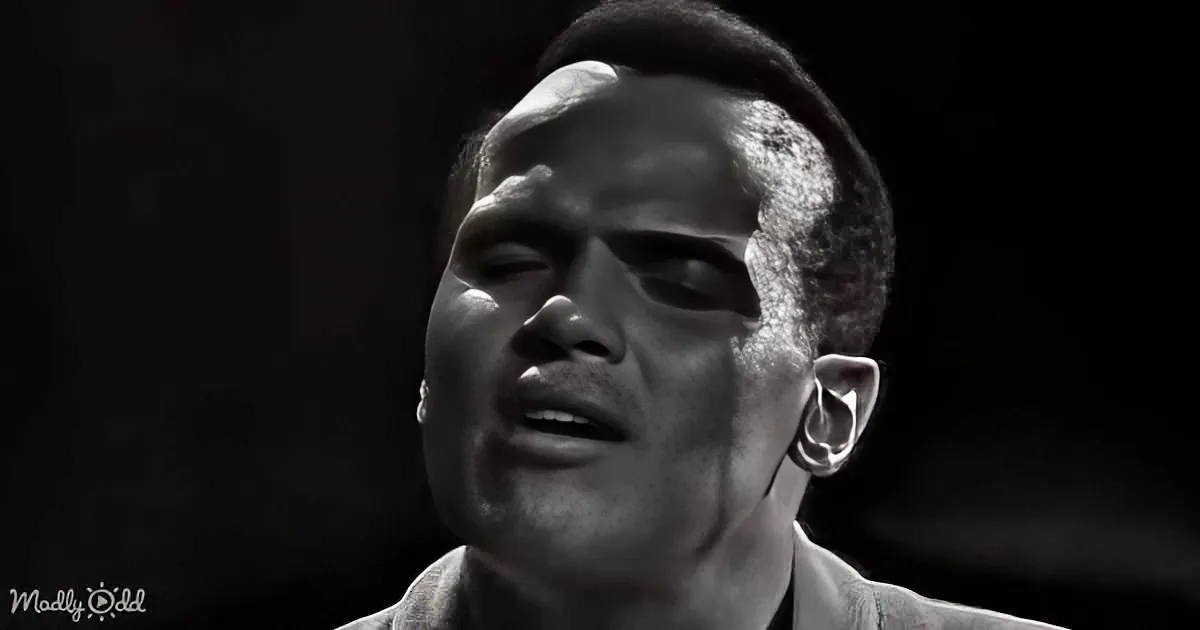 A man with short hair, wearing a light-colored shirt, is shown in a close-up with a dark background.