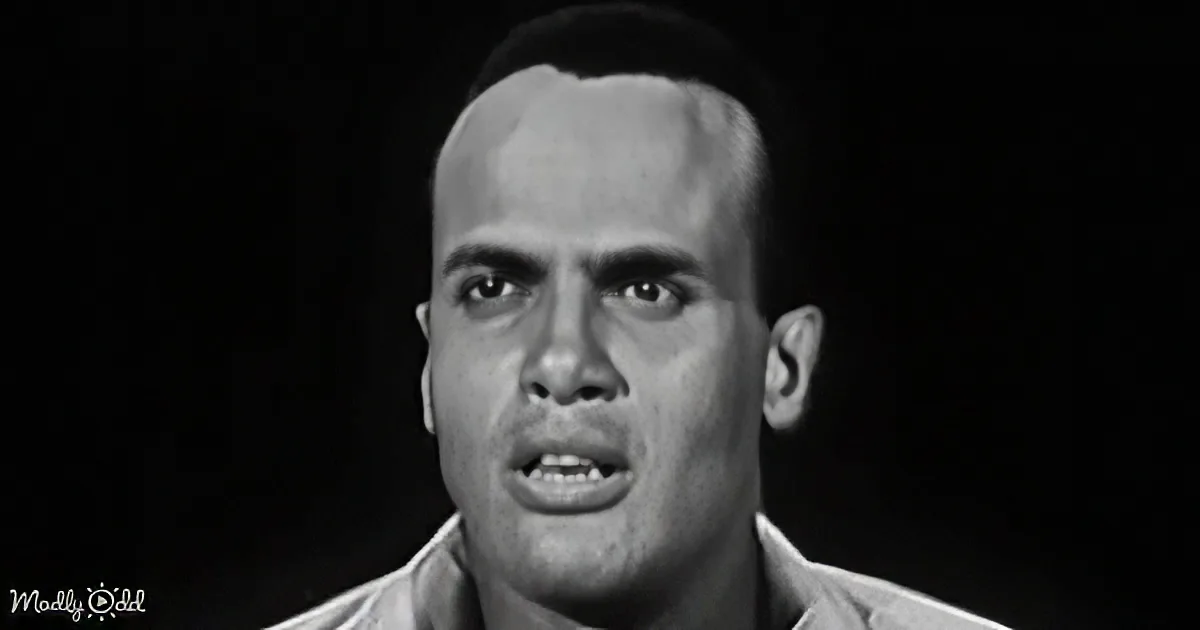 A man with a serious expression, wearing a light-colored shirt, against a dark background.