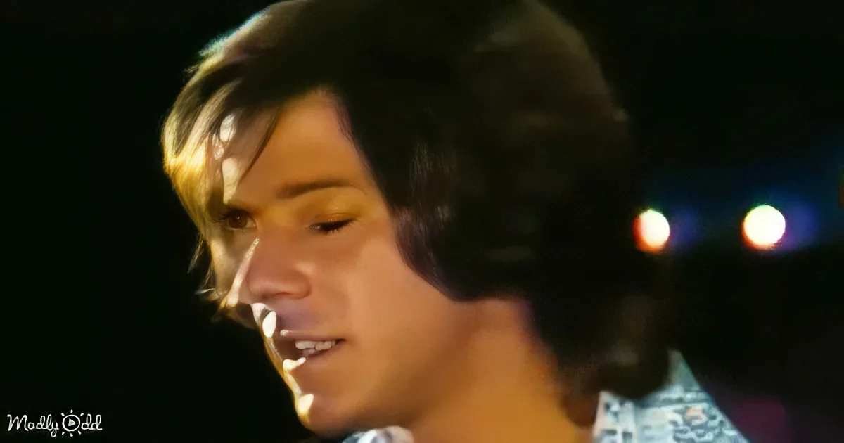 A person with long, dark hair and a light-colored shirt is shown in a close-up, with blurred lights in the background.