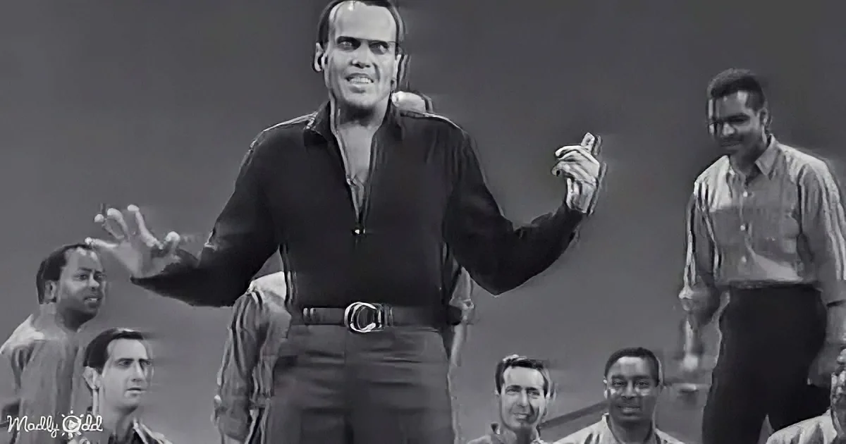 A man in a black shirt gestures dramatically, surrounded by a group of people in a dimly lit setting.