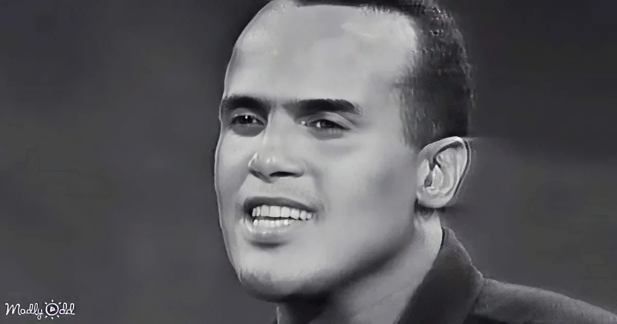 A man with a receding hairline and a slight smile, wearing a dark shirt, against a dark background.