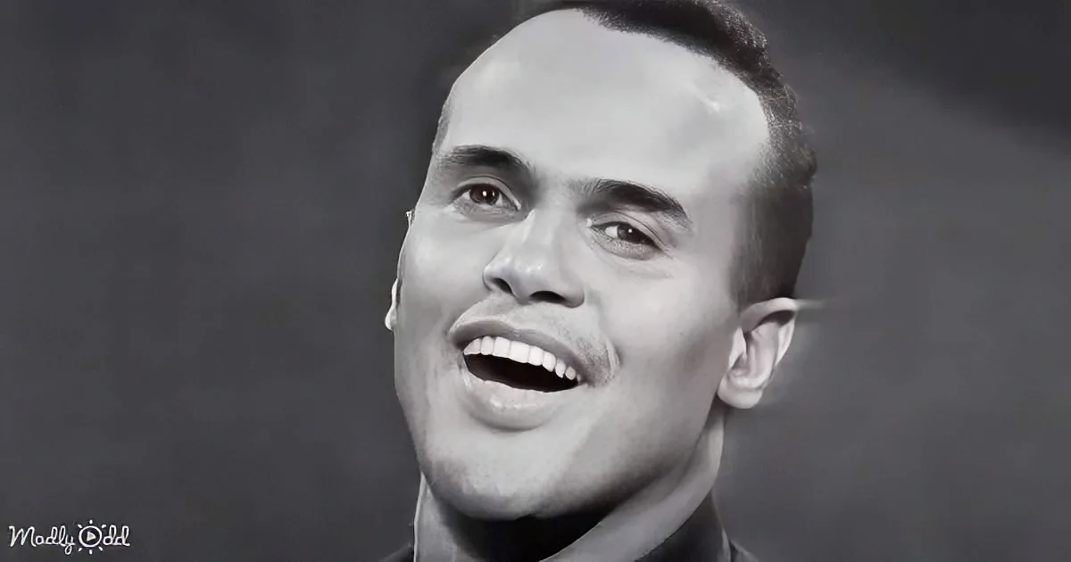 A man with a receding hairline and a wide smile, wearing a dark shirt, against a dark background.