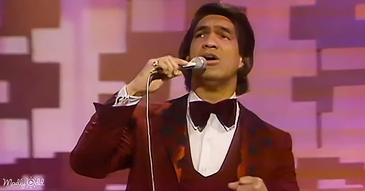 A man in a red suit with a bow tie sings into a microphone on stage.