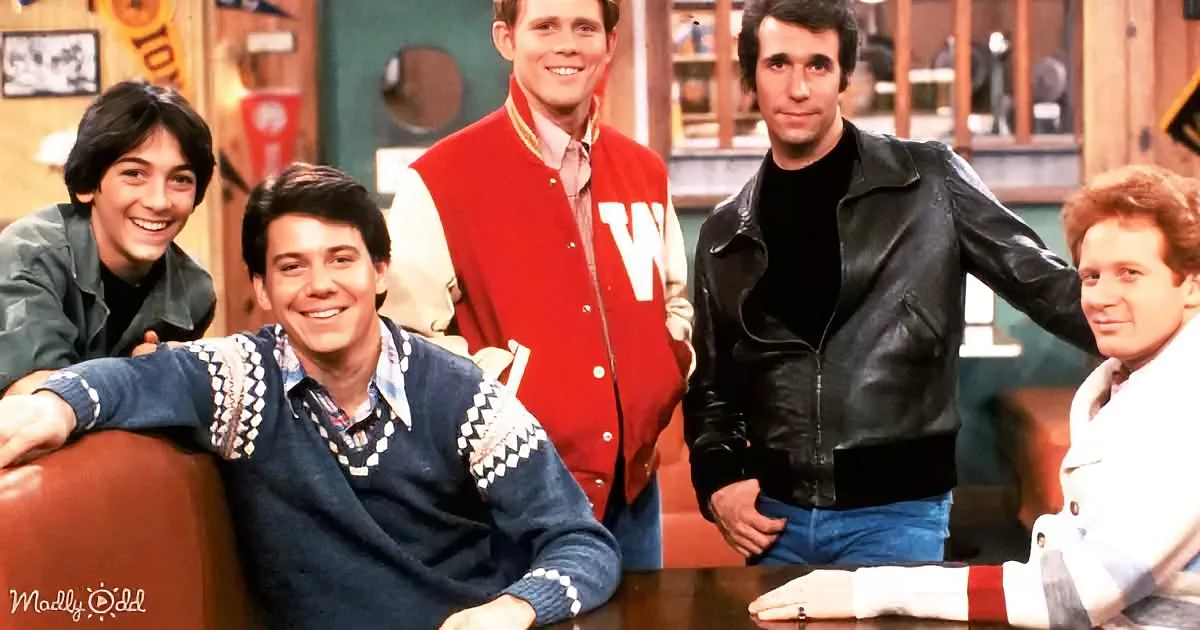 A man in a blue sweater vest smiles while others in casual attire pose in a room with a bar.
