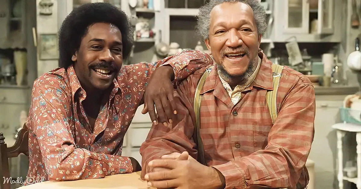 Two men in a kitchen, one in a floral shirt, the other in a plaid shirt, both smiling.