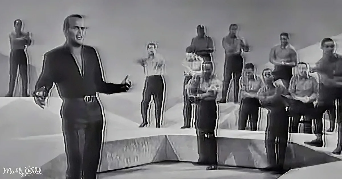 A man in a suit gestures while standing in front of a group of people in athletic attire.