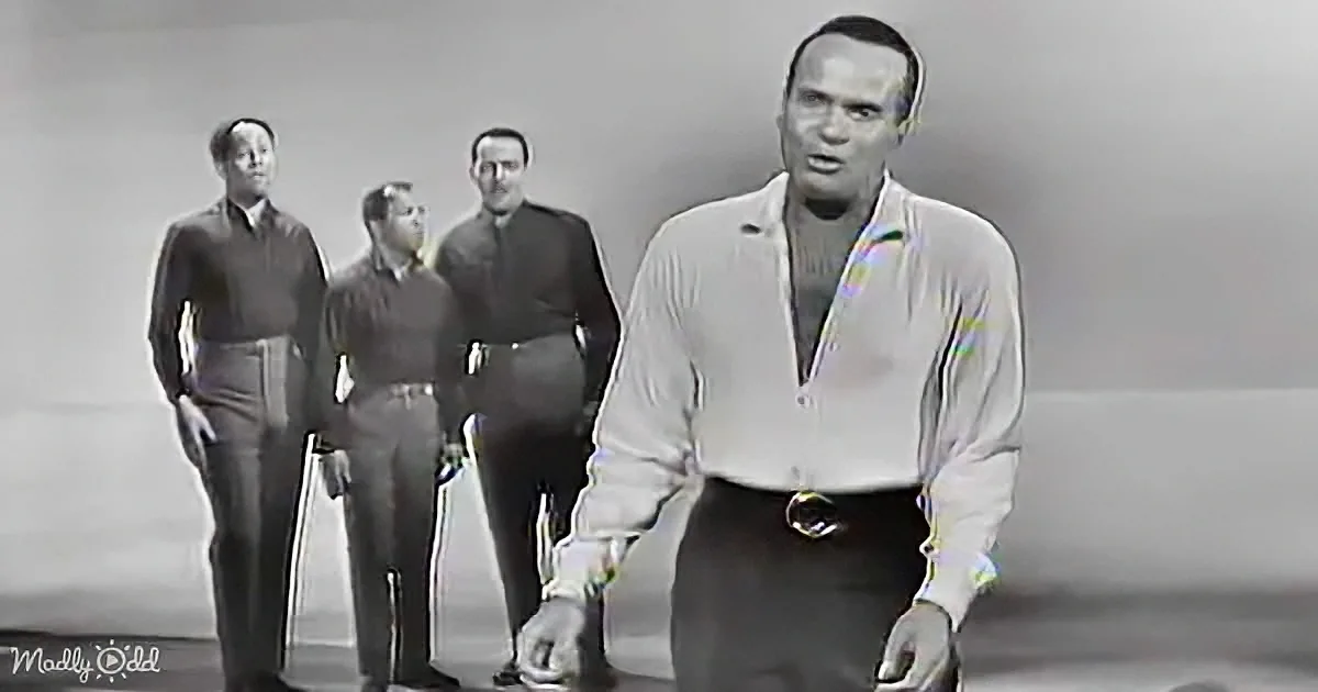 A man in a white shirt and dark pants stands in front of three other men in a studio setting.