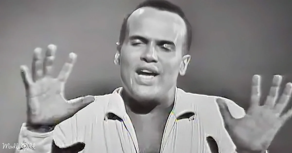 A man in a white shirt with his hands raised, appearing to sing or express something.