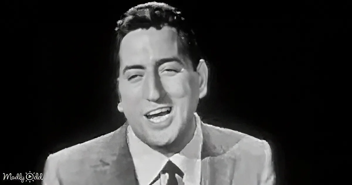 A man in a suit and tie smiles, eyes closed, against a dark background.
