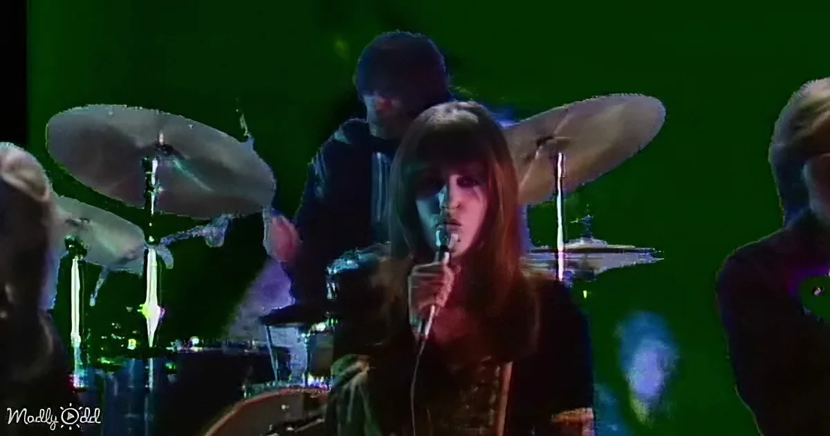 A woman sings into a microphone on stage with a drummer behind her.