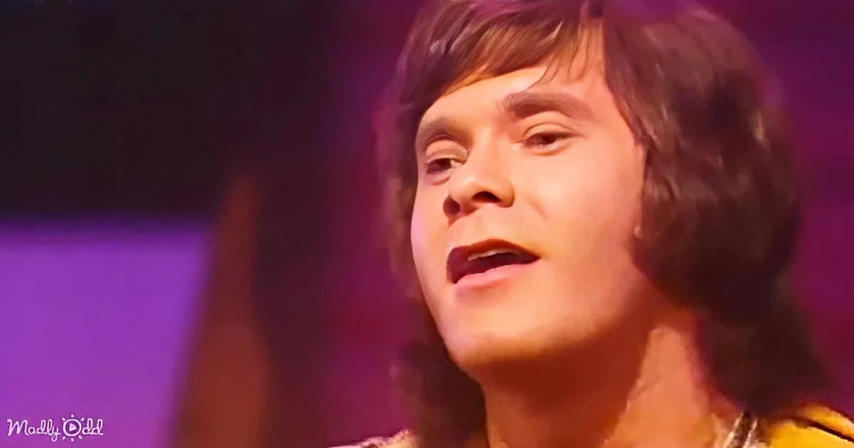 A person with shoulder-length hair, wearing a yellow top, is captured in a close-up shot against a purple-lit background.