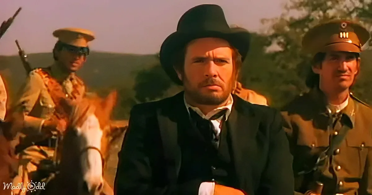 A man in a black suit and hat sits with soldiers in uniform, suggesting a historical or dramatic scene.