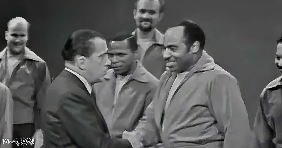 Two men in suits are engaged in conversation, surrounded by other individuals in a formal setting.