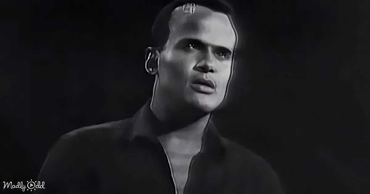 A man with a bald head and a serious expression, wearing a dark jacket, stands against a dark background.