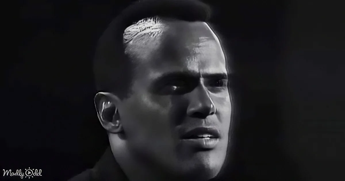A man with a serious expression, his face illuminated against a dark background.