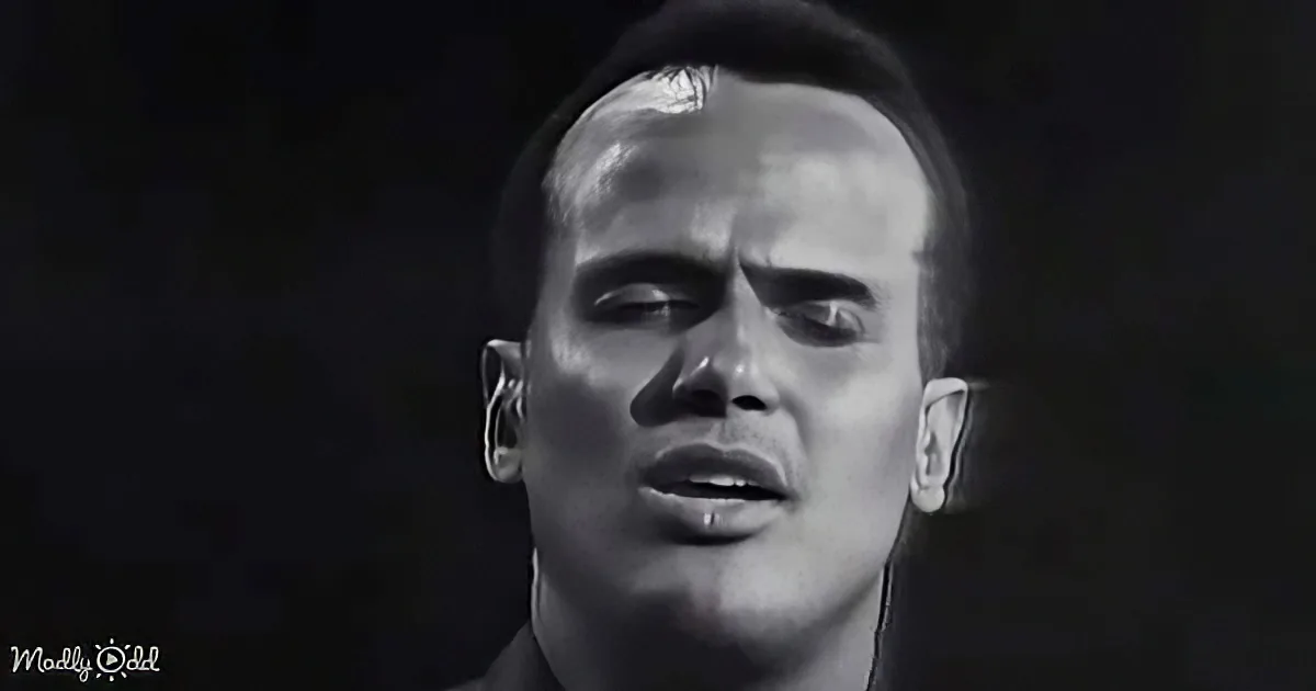 A person with short hair, closed eyes, and a piercing in their lower lip is shown against a dark background.
