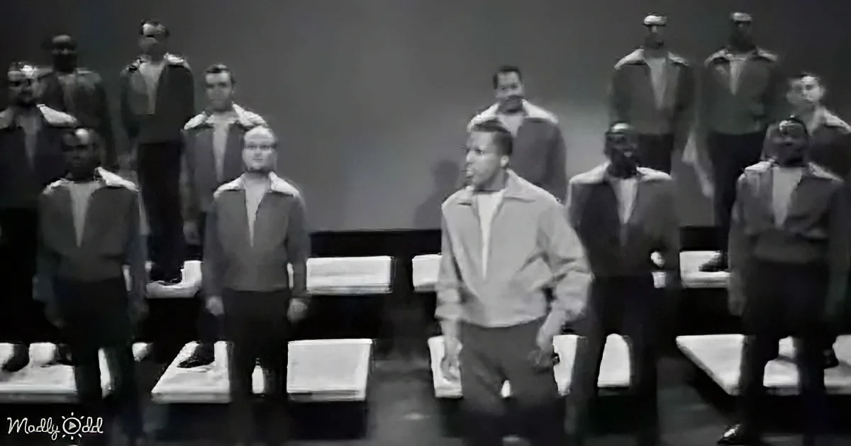 A man in a light jacket walks past a group of uniformed individuals in a dimly lit room.