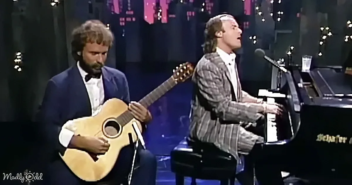 A man plays piano while another sings and plays guitar on stage.