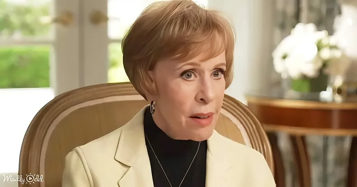 A woman with short blonde hair, wearing a light-colored blazer and black top, sits in a chair, looking slightly to the side.