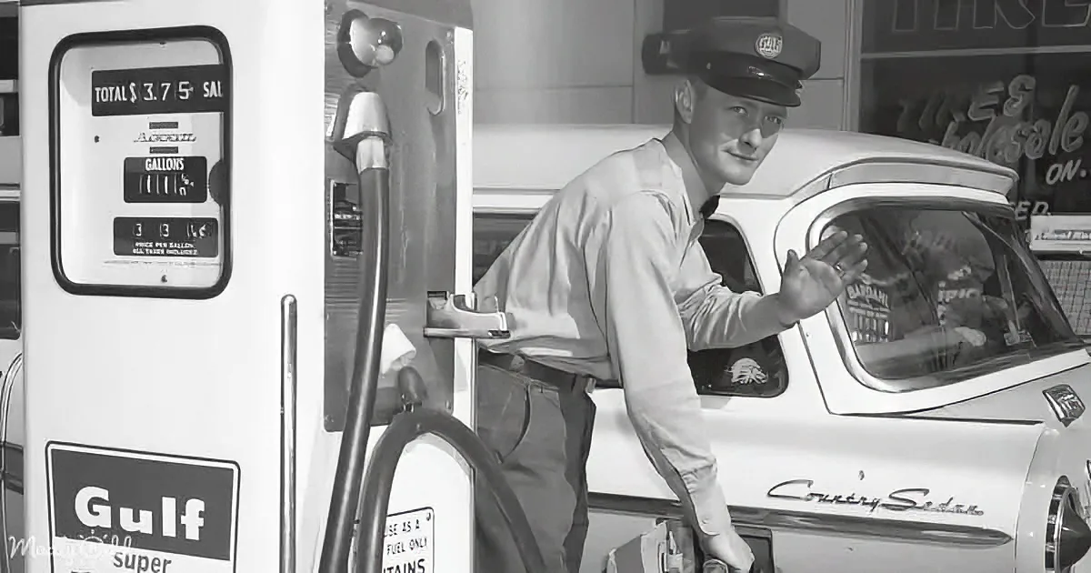 A man in a uniform at a Gulf gas station, pumping gas into a white car.