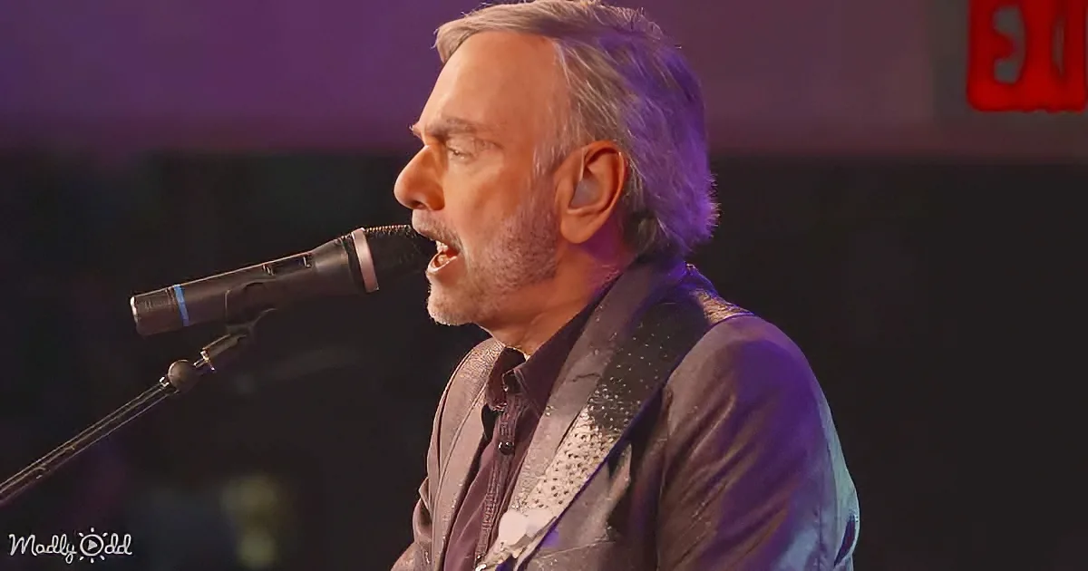 A man with gray hair and beard sings into a microphone, wearing a black jacket and white shirt.