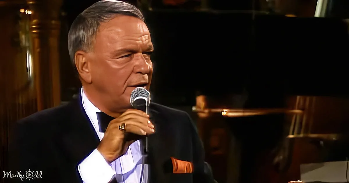 A man in a suit sings into a microphone, wearing a ring and a pocket square.